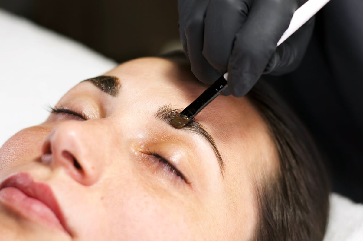 Close-up of a beautician applying eyebrow tint to a woman's brows during a professional brow lamination treatment