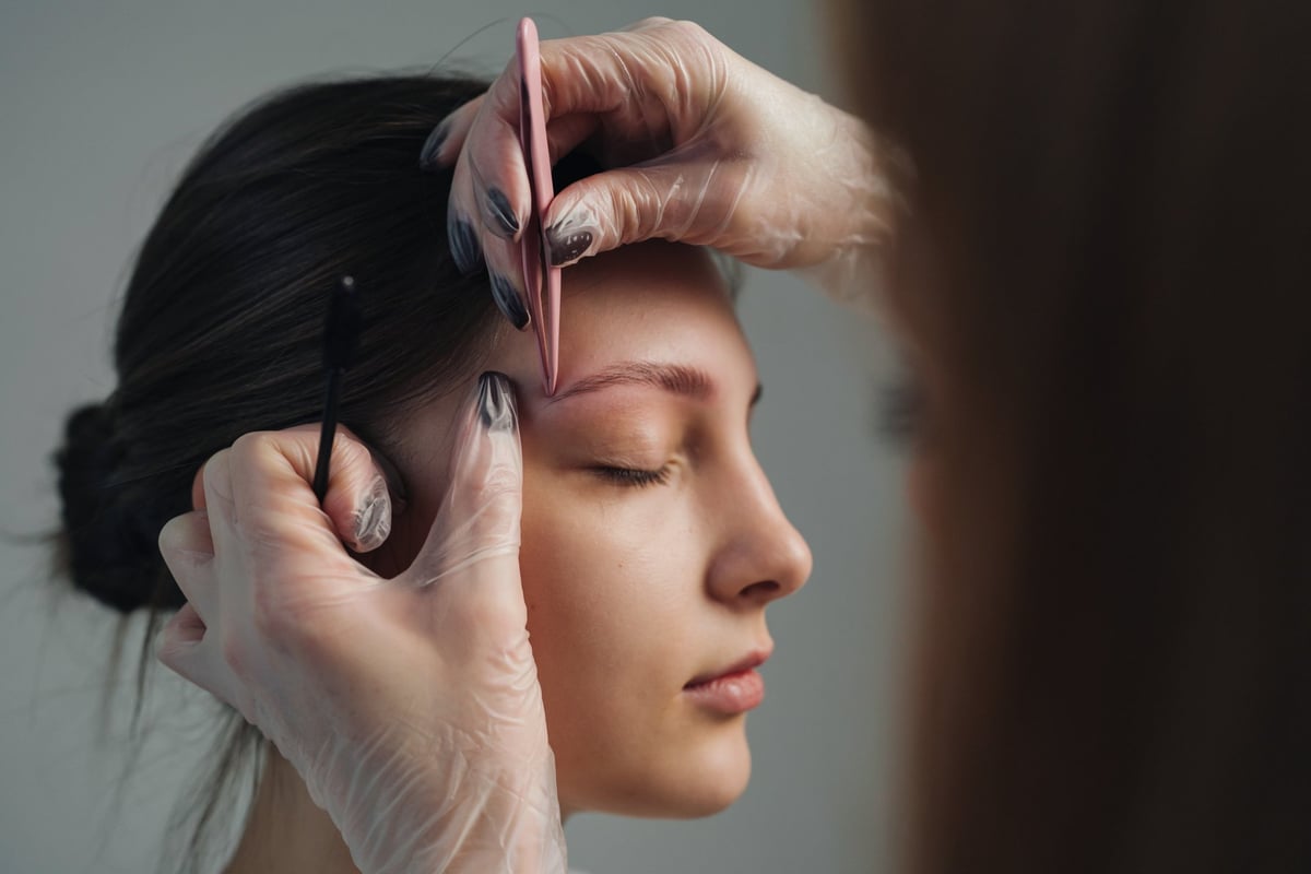 Close-up eyebrow shaping by experienced esthetician using tweezers
