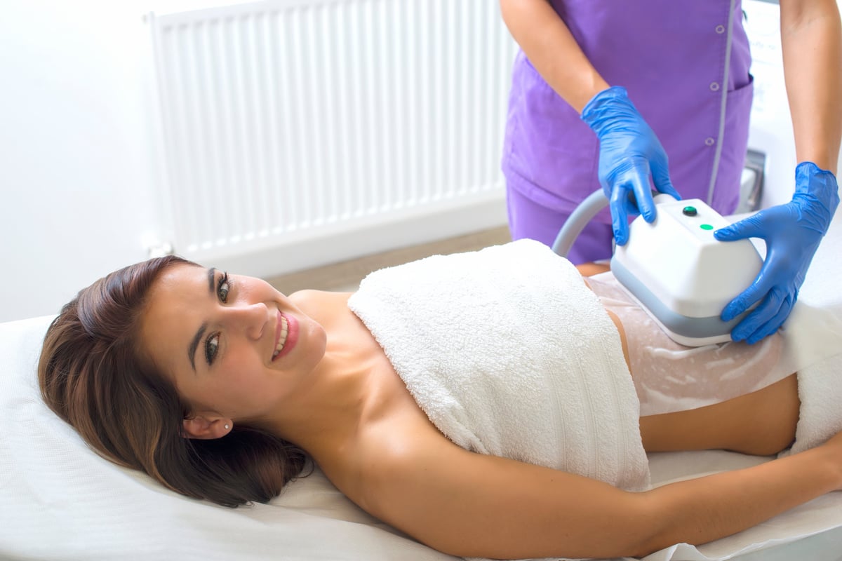 Woman receiving ultrasound treatment on abdomen from healthcare provider wearing purple uniform and blue gloves